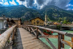 Wooden bridge over mountain river as houses and old church on background in small town of Gressoney-Saint-Jean in Aosta Valley, Italy.