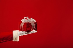 Christmas. Photo of Santa Claus gloved hand with red gift box, on a red background
