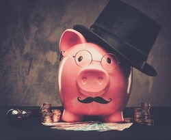 Piggybank in glasses and hat with pile of coins and banknotes 