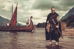 Viking warrior with sword standing near Drakkar on the seashore.
