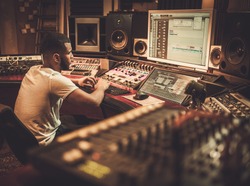 African american sound engineer working at mixing panel in boutique recording studio.