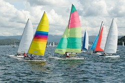 Children sailing in small boats and dinghies with colourful sails for fun and competition. Teamwork by junior sailors racing on saltwater Lake Macquarie. Photo for commercial use.