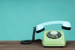 Old telephone on wooden table in front of green background. Vintage phone with taken off receiver. Vintage style photo. 