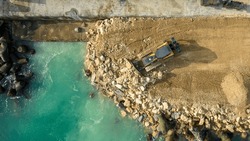 Aerial view of waterfront construction site with excavator. Bulldozer working on a breakwater construction