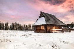 Traditional Wooden House in Winter Woods at Sunset.