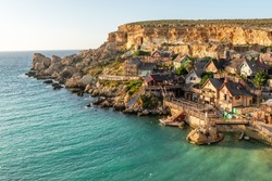 Malta, Il-Mellieha. View of the famous Popeye Village in Anchor Bay. Turquoise sea waters, blue sky and sunset light on cliffs.