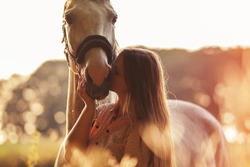 Woman kissing her horse at sunset, autumn outdoors scene