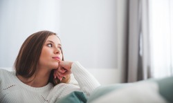 Sad woman sitting on sofa at home deep in thoughts, thinking about important things