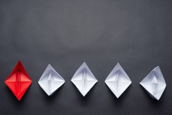 Row of paper ships on black background. Business concept of creative innovation and leadership. Flat lay red origami boat in group of white boats. Corporate strategy and successful solution.