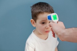 using infrared thermometer to measure child's body temperature on a blue background