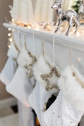 White Christmas socks and silver stars with bells hanging on fireplace. Christmas gifts in socks