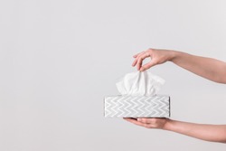 Delicate female hands pulling a tissue out of a gray tissue box.