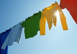 Colorful clothes hanging to dry on a laundry line and sun shining in the blue sky.