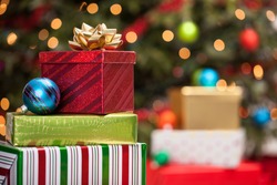 Stacks of Christmas presents under a Christmas tree with defocused lights