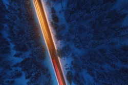 Top down view to road in the snowy wood. Romantic night aerial photo of cars traveling on the mountain road.