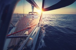 Sunset at the Sailboat deck while cruising / sailing at opened sea. Yacht with full sails up at the end of windy day. Sailing theme - background. Yachting background design.