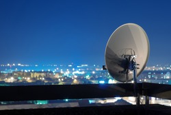 Satellite dish antenna on top of the building in urban area at night.