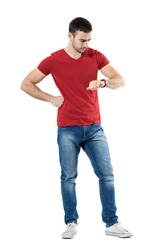 Young upset casual man waiting for someone checking time on wrist watch. Full body length portrait isolated over white studio background.