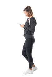 Side view of young happy fit runner woman using mobile phone and smiling. Full body length portrait isolated on white background. 