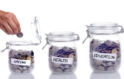 Saving, Health and Education concept: Glass jar with coin and hand putting the coin into the jar
