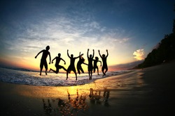 Friends jumping for joy on tropical beach at sunset in a group formation