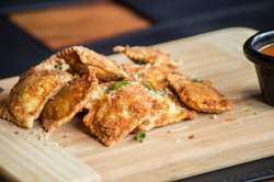 Fried Ravioli served on wooden board on a table accompanied natural tomato sauce.