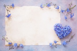 Heart made of forget-me-not flowers on a decorative background and old paper for text, greetings.