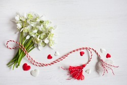 A bouquet of snowdrops flowers, red and white rope with tassels, hearts on a wooden background. Postcard for the holiday of March 1, space for text.