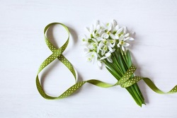 Geeting card for Women's day march 8, number eight from a green ribbon and a bouquet of snowdrops on a white wooden background