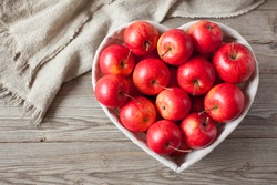  Red apples in a heart shaped basket on a wooden background.