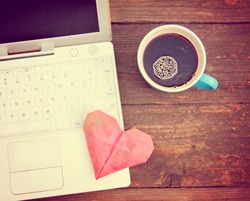  Laptop or notebook with cup of coffee and origami heart on old wooden table toned with a retro vintage instagram filter 