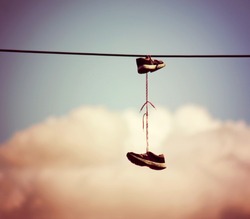  sneakers hanging from electrical wire against a blue sky with clouds toned with a retro vintage instagram filter effect 