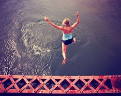  a girl jumping of an old train trestle bridge into a river toned during summer time toned with a retro vintage instagram filter effect