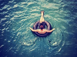 a man floating down a river in a blow up tube with a baseball cap on and shorts on a hot summer day from overhead toned with a retro vintage instagram filter effect