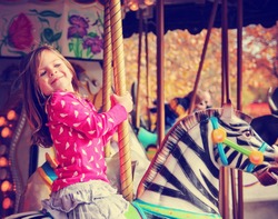  a young girl riding on a merry go round at the zoo toned with a retro vintage instagram filter effect app or action