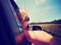 a woman with her head out the window enjoying a scenic drive through the sawtooth mountain range in idaho along an old highway toned with a retro vintage instagram filter app or action effect