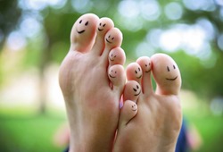 smiley faces on a pair of feet on all ten toes in a park on a hot summer day 
