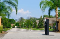 Entrance gate to a beautiful gated residential house community with lush green trees and grass