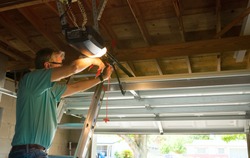 Professional automatic garage door opener repair service technician man working on a ladder at a home residential location making adjustments and fixing it while installing it.