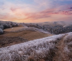 Winter coming. Picturesque pre sunrise scene above late autumn mountain countryside with hoarfrost on grasses, trees, slopes. Peaceful sunlight rays from cloudy sky. Ukraine, Carpathian Mountains.