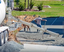 Unidentifiable hispanic men working on a new concrete driveway at a residential home, focus on concrete chute