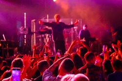 Anonymous people raising arms and dancing under red neon illumination near stage with band during music show