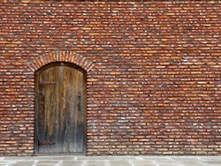 Full frame of bright red colored masonry wall with arched door of shabby wood