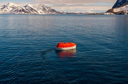 Lowering orange lifeboat to water in Arctic waters, Svalbard. Abandon ship drill. Lifeboat training. Man over board drill.
