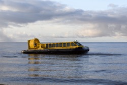 Hovercraft flying above water. Air cushion sailing near beach. Yellow hover craft under way.