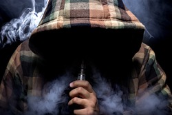 Man with concealed identity smoking a controversial vape.  Vaping is debatable in the health community if it is safe or a health risk. 