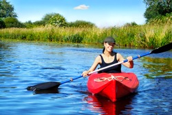 Girl with paddle and kayak on a small river in rural landscape