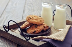 Chocolate chip cookies  with  milk in bottles on wooden tray