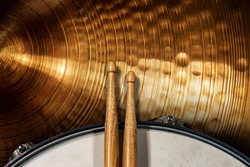 Close-up of two wooden drumsticks on an old metallic snare drum and golden colored cymbal with copy space. Percussion instrument