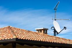 Closeup of a Television Aerial and Satellite Dish on the House Roof on blue sky with clouds